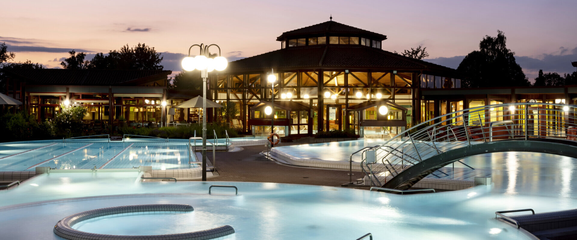 badsaulgauerleben-sonnenhoftherme-aussenansichtnacht Thermalbad Sonnenhof-Therme bei Dämmerung mit beleuchteten Außenpools, einem modernen Gebäude im Hintergrund und entspannter Atmosphäre.