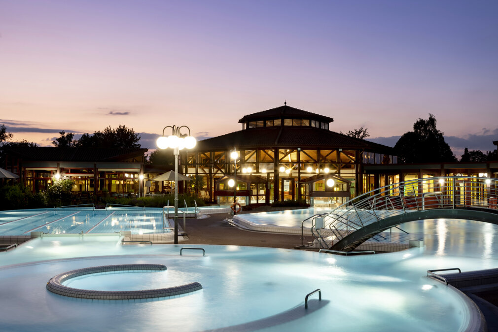 badsaulgauerleben-sonnenhoftherme-aussenansichtnacht Thermalbad Sonnenhof-Therme bei Dämmerung mit beleuchteten Außenpools, einem modernen Gebäude im Hintergrund und entspannter Atmosphäre.