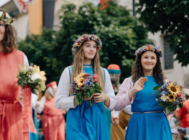 Frauen in Kleidern mit Blumenkränzen auf dem Kopf.