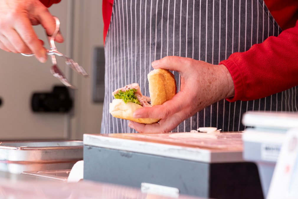 Ein Verkäufer bereiten ein belegtes Brötchen am Wochenmarkt vor.