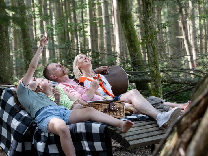 Eine Familie entspannt auf einer Liege im Wald.