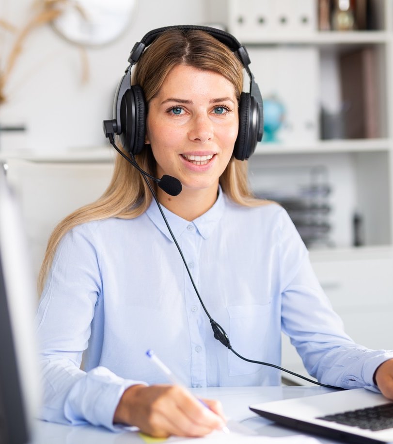 Eine Frau sitzt mit einem Headset vor einem Laptop.