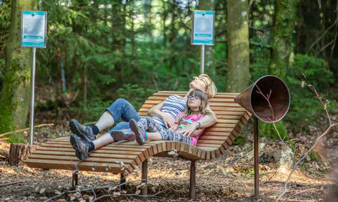 Eine Mutter und ihre Tochter entspannen gemeinsam auf einer Holzliege im Wald.